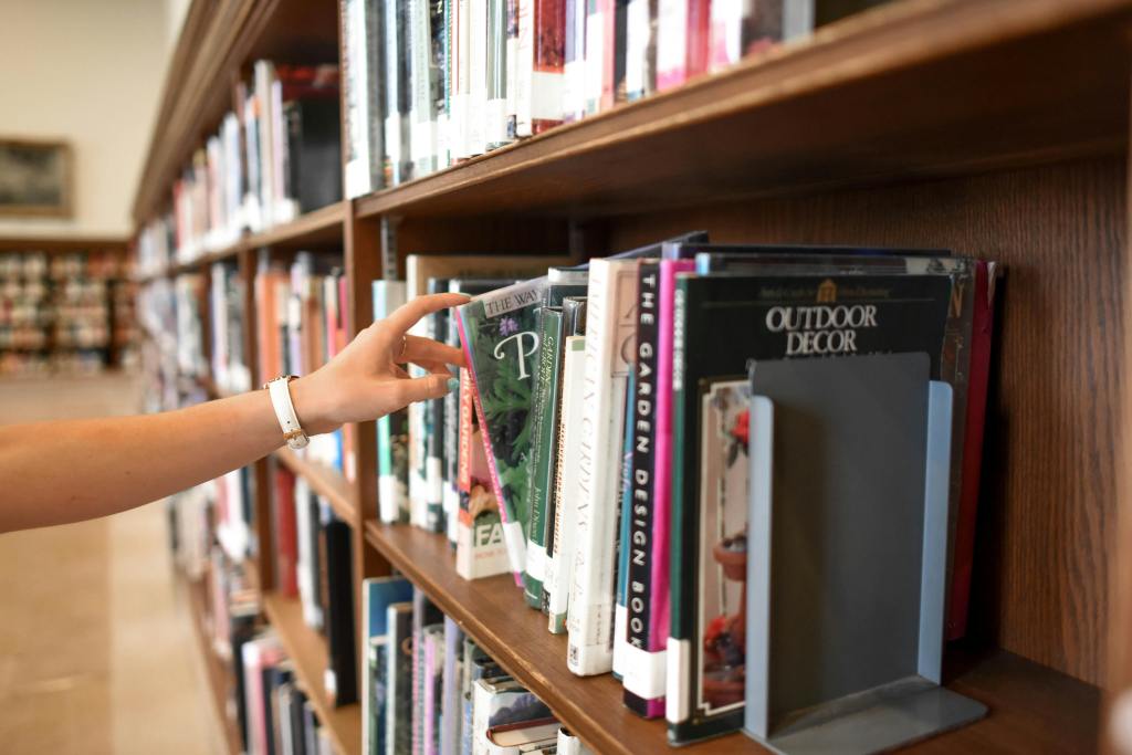 stack of library books and a person reaching for a book