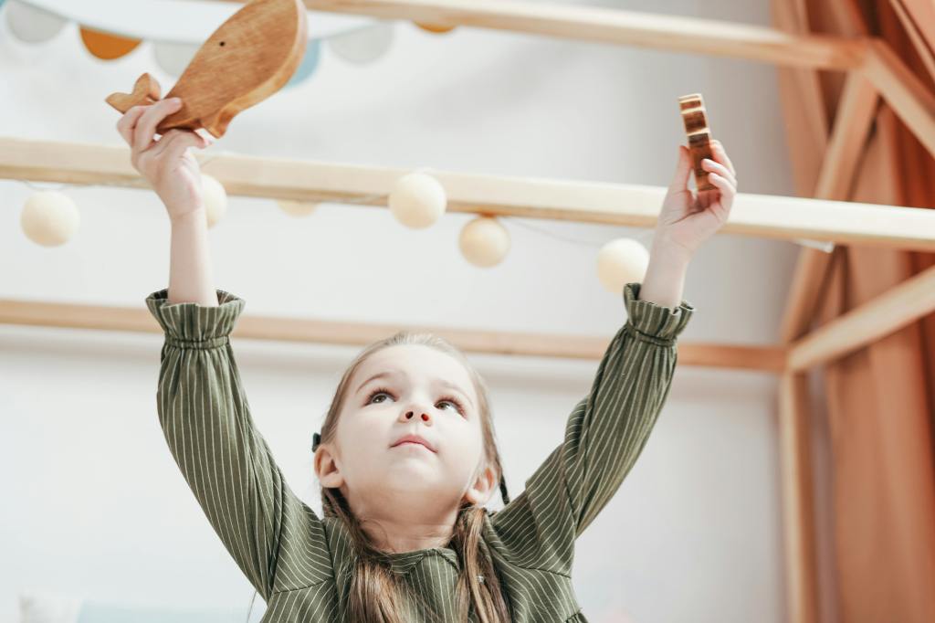little girl playing and holding a wooden whale toy in the air