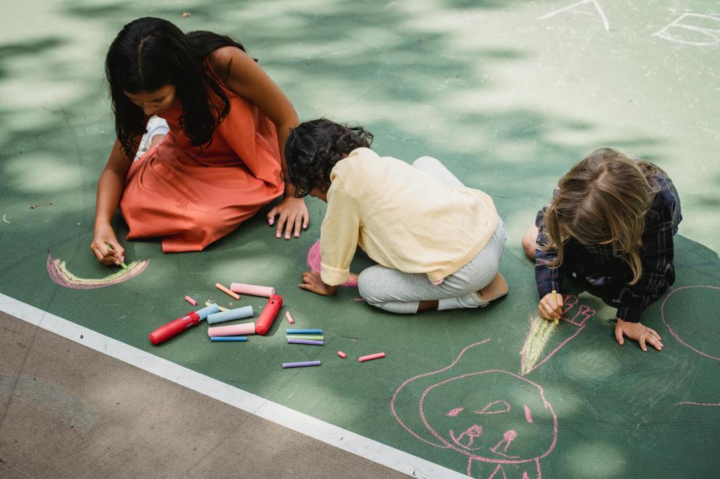 three girls drawing chalk murals on the ground