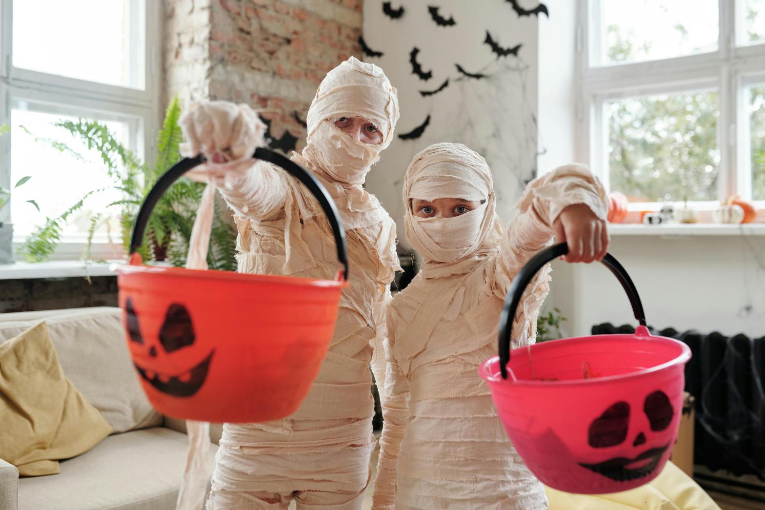 two kids dressed as mummies carrying pumpkin buckets
