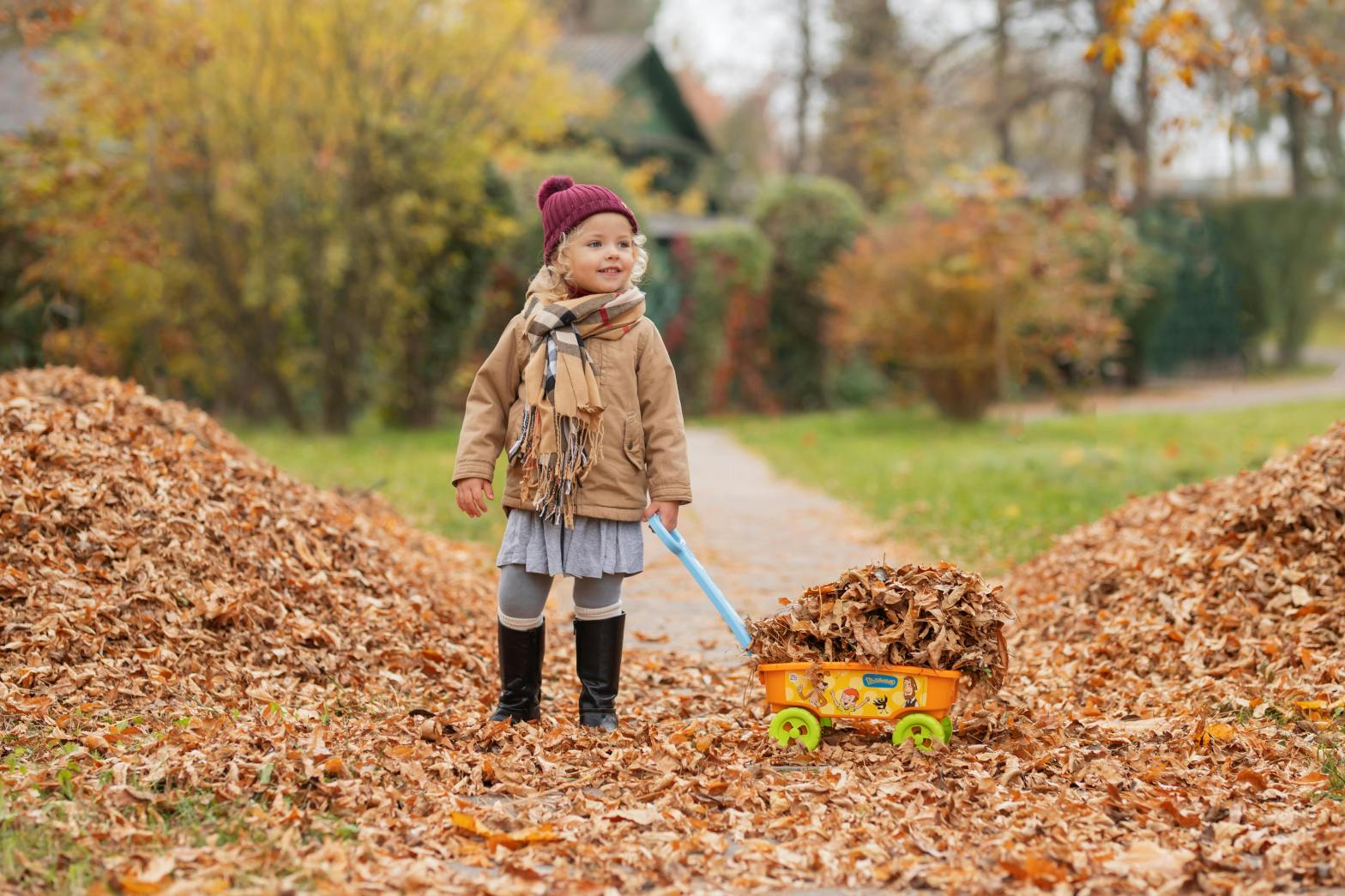 a small girl next to leave piles while pulling a wagon full of leaves
