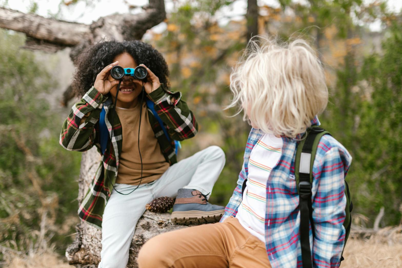 a girl and boy outside. the girl is looking through binoculars.